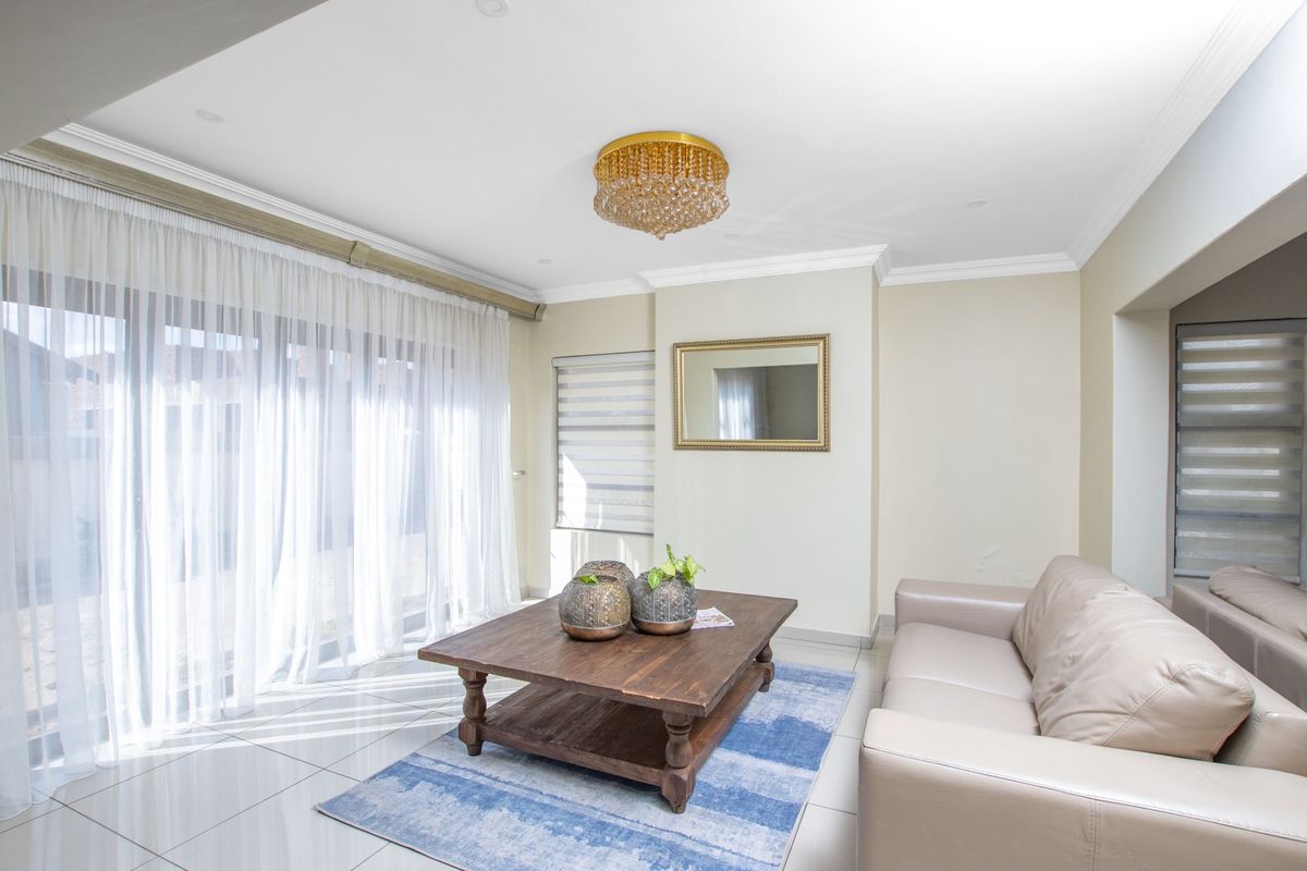 A bright and well-maintained living room featuring large sliding glass doors, tiled flooring, crown molding, and a decorative crystal chandelier.