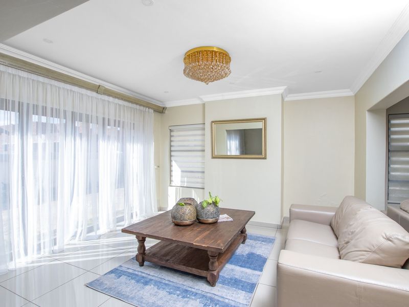 A bright and well-maintained living room featuring large sliding glass doors, tiled flooring, crown molding, and a decorative crystal chandelier.