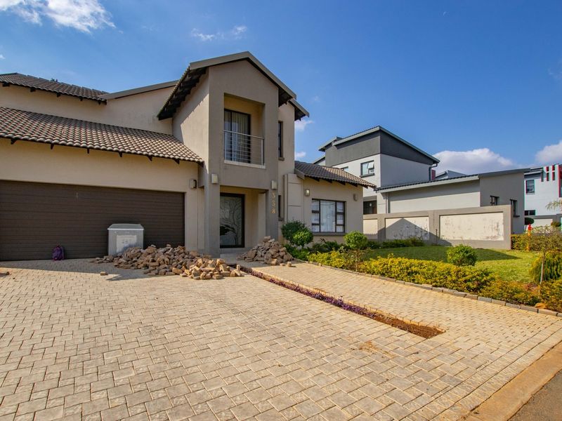 Front elevation of a double-story house featuring a paved driveway, double garage, balcony, and a landscaped garden area.