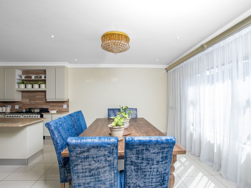 An open-plan dining area featuring tiled floors, crown molding, and a modern kitchen with granite countertops and built-in cabinetry.