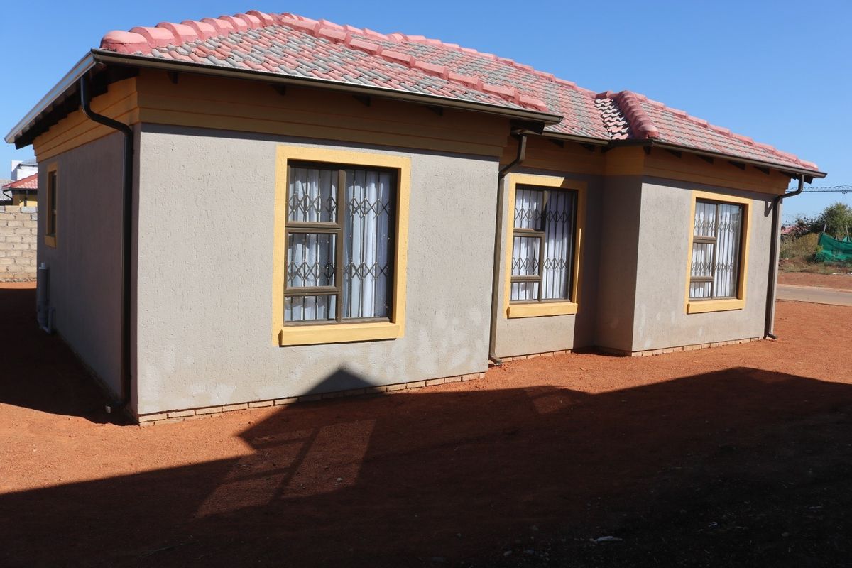 Rear view of a single-story house featuring a tiled roof, plastered walls with yellow trim, and security bars on the windows.
