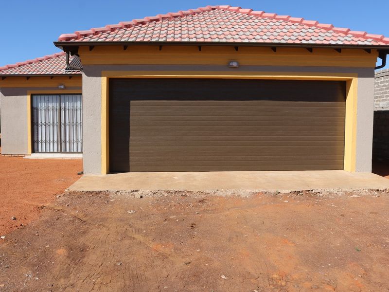 Front view of a residential property featuring a single garage door, tiled roof, and security gate, with unfinished landscaping in the foreground.