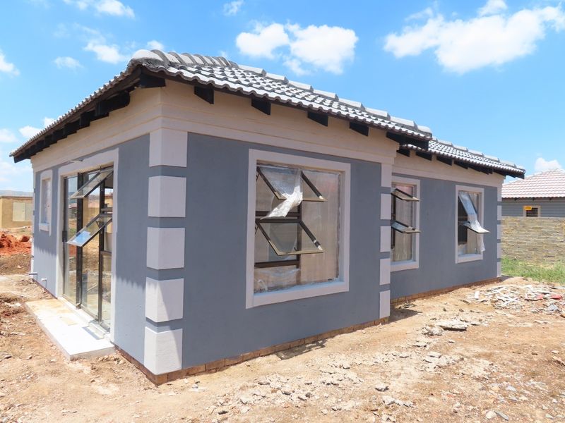 Newly constructed house exterior featuring a tiled roof, grey plastered walls with white corner detailing, and modern aluminium window frames.