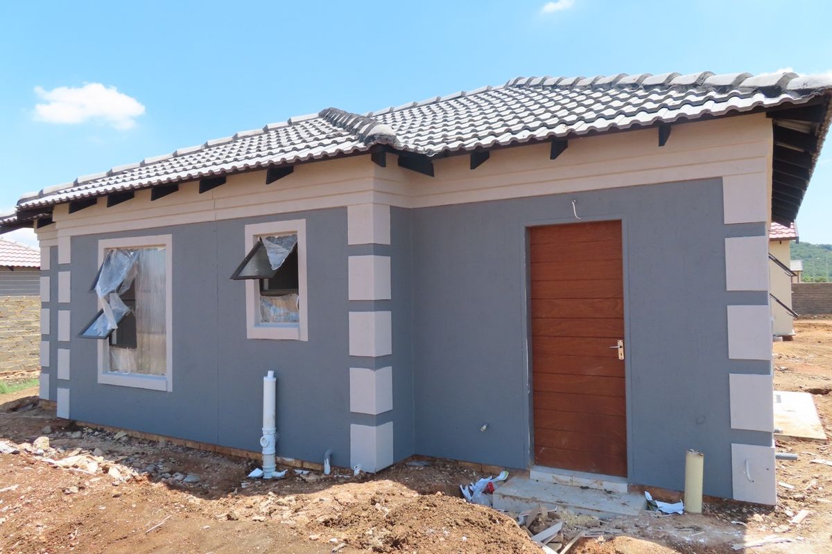 A newly constructed single-story house featuring a grey facade with contrasting trim, a timber entrance door, and tiled roofing, currently undergoing final site completion.