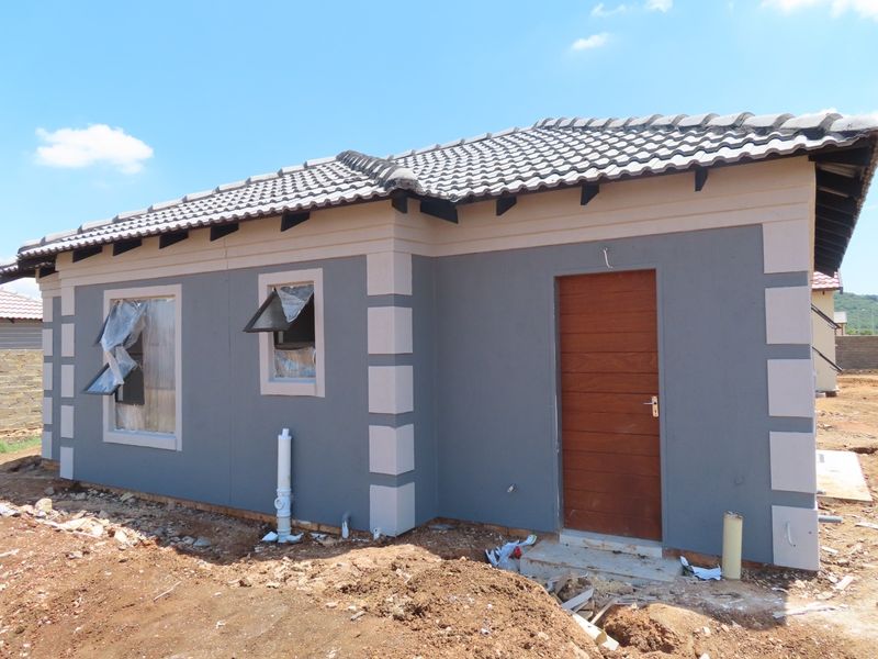 A newly constructed single-story house featuring a grey facade with contrasting trim, a timber entrance door, and tiled roofing, currently undergoing final site completion.