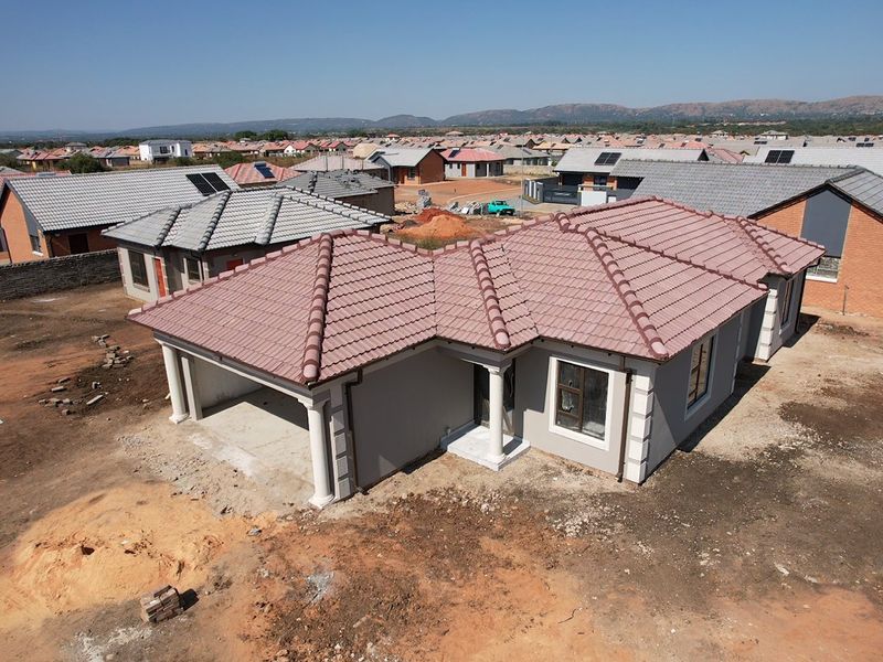 Aerial view of a newly constructed single-story house featuring a tiled roof, integrated garage, and unfinished surrounding grounds in a residential estate.
