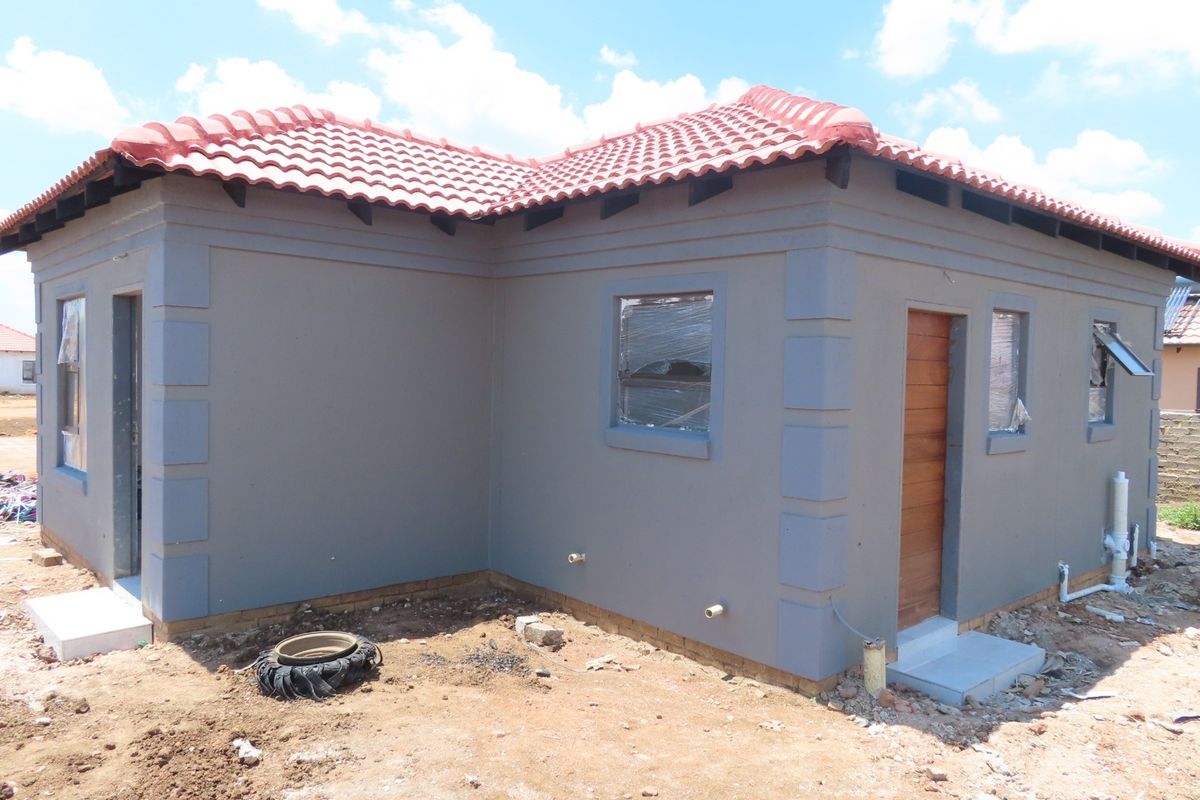 A newly constructed single-story house featuring a grey plastered facade, terracotta tiled roof, and timber entrance door, currently undergoing final exterior site completion.