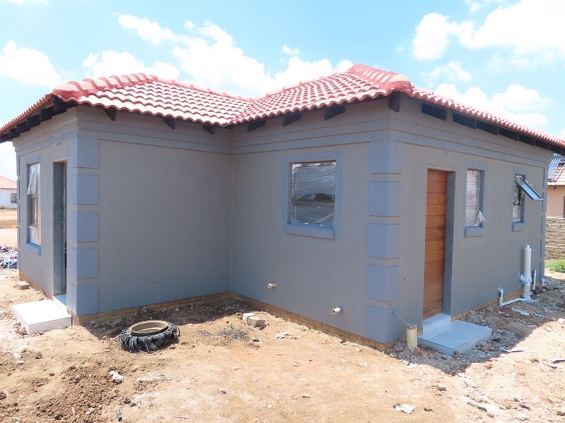 A newly constructed single-story house featuring a grey plastered facade, terracotta tiled roof, and timber entrance door, currently undergoing final exterior site completion.
