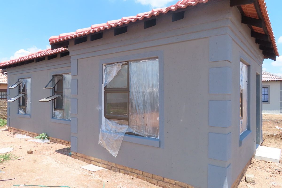 A newly constructed house exterior featuring grey plastered walls, terracotta roof tiles, and aluminium window frames, currently in the final stages of completion.