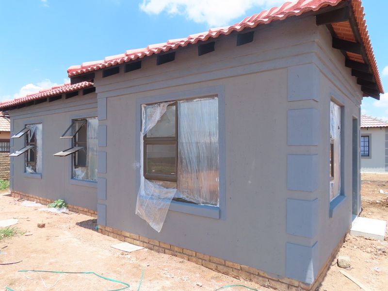 A newly constructed house exterior featuring grey plastered walls, terracotta roof tiles, and aluminium window frames, currently in the final stages of completion.