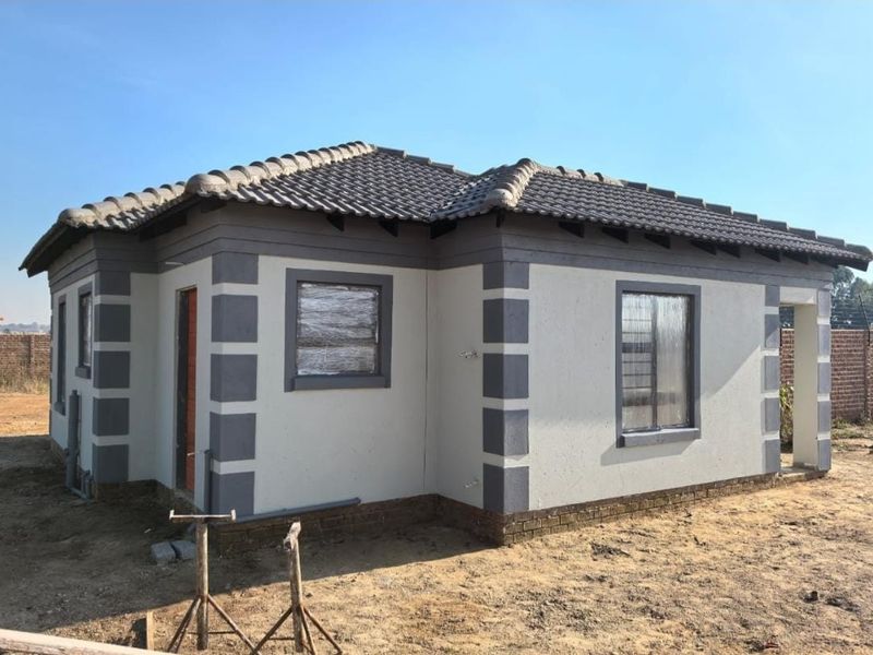 A newly constructed single-story house featuring a tiled roof, plastered exterior walls with contrasting corner detailing, and aluminium window frames.