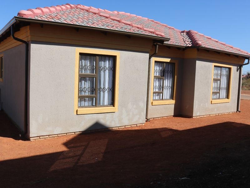 Rear view of a single-story house featuring a tiled roof, plastered walls with yellow trim, and security bars on the windows.
