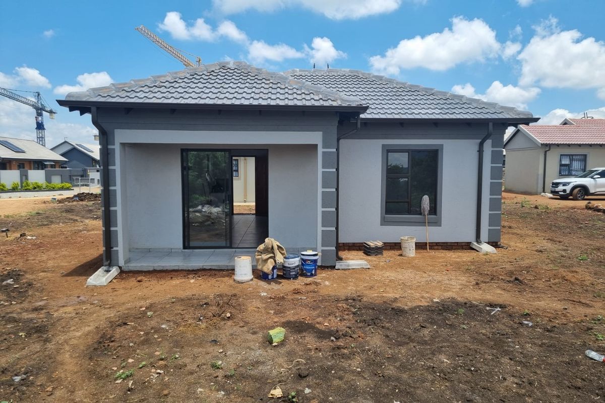 A newly constructed house exterior featuring a tiled roof, aluminium window frames, and a covered patio area, currently awaiting final landscaping.