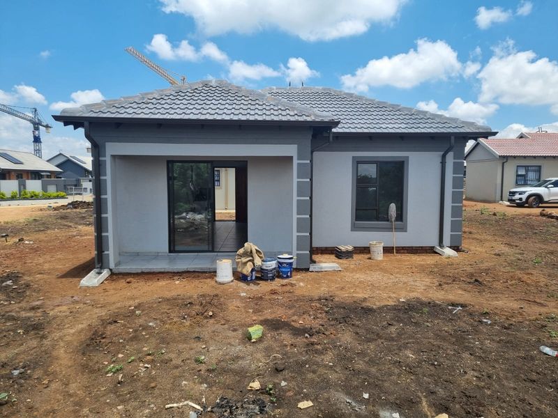 A newly constructed house exterior featuring a tiled roof, aluminium window frames, and a covered patio area, currently awaiting final landscaping.