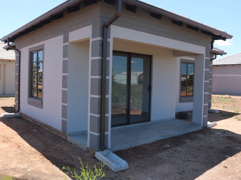 A modern residential exterior featuring a covered tiled patio, sliding glass doors, and aluminium window frames, set within an unfinished garden area.