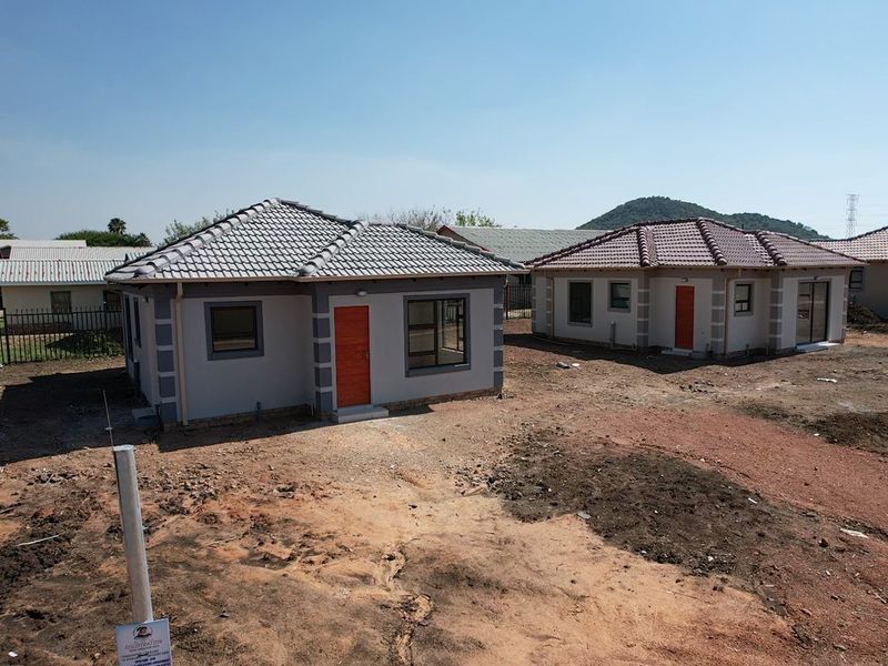 An elevated view of newly constructed residential houses featuring tiled roofs, grey exterior walls, and orange entrance doors set on an undeveloped plot.