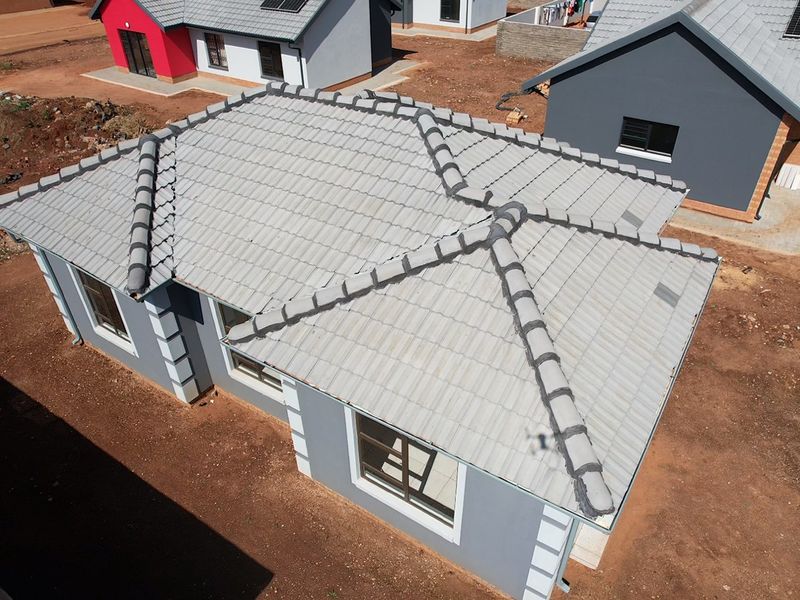 Aerial view of a modern residential house featuring a grey tiled roof, plastered exterior walls, and aluminium window frames in a new development.