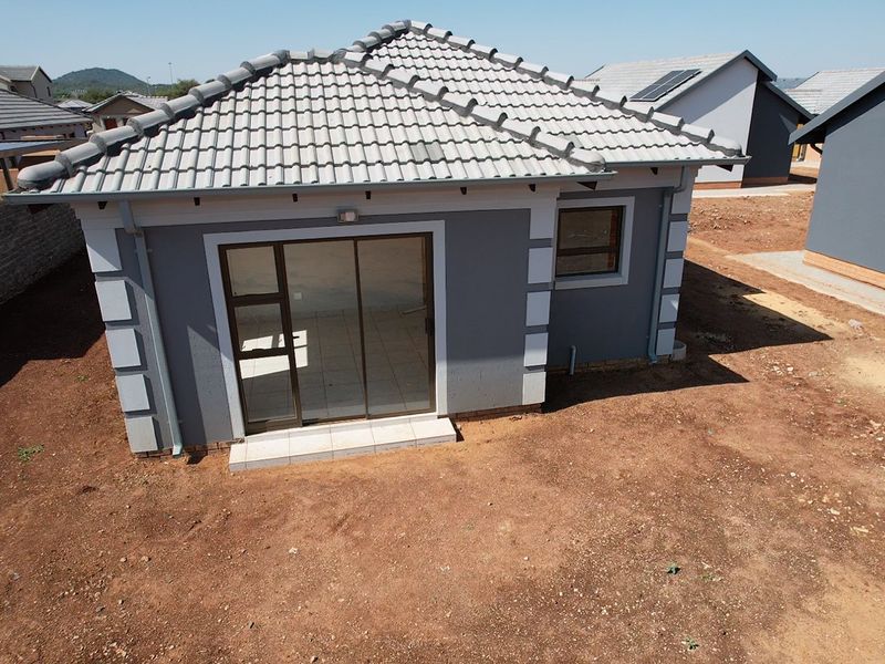 Aerial view of the rear elevation of a modern grey house featuring a tiled roof, sliding glass door, and an unlandscaped garden area.