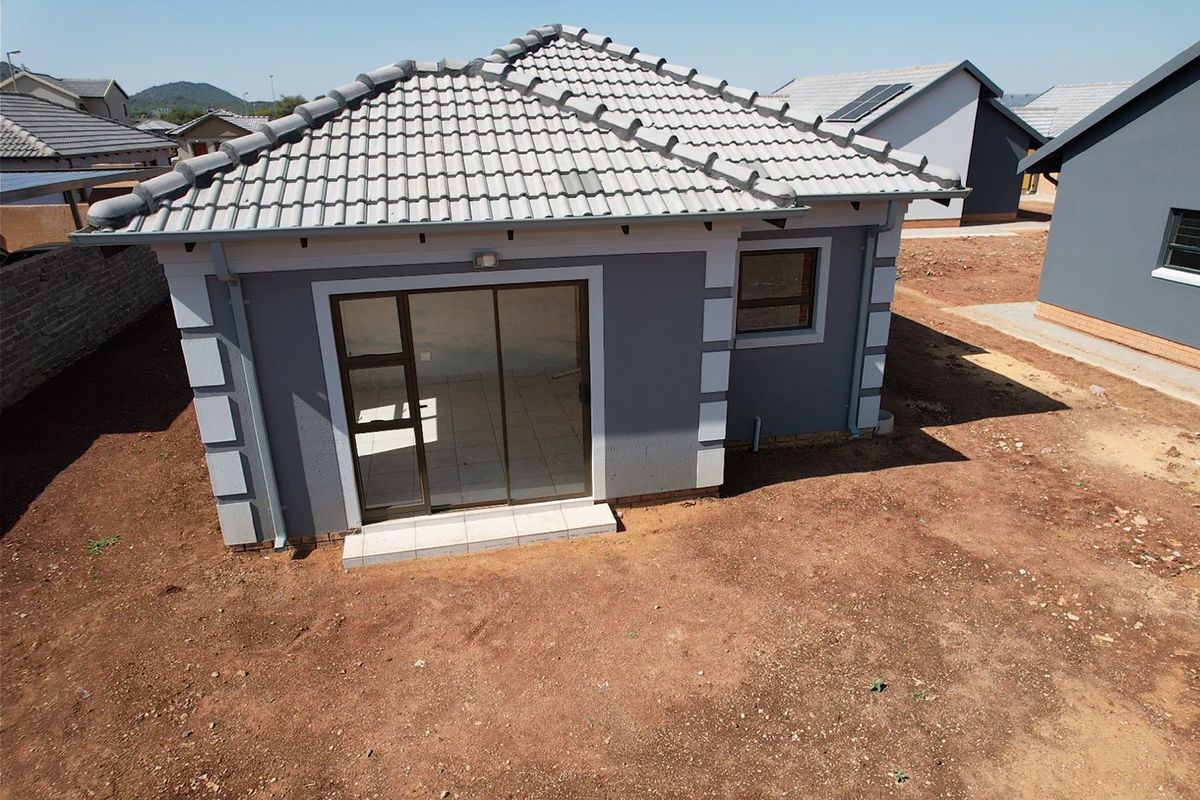 Aerial view of the rear elevation of a modern grey house featuring a tiled roof, sliding glass door, and an unlandscaped garden area.