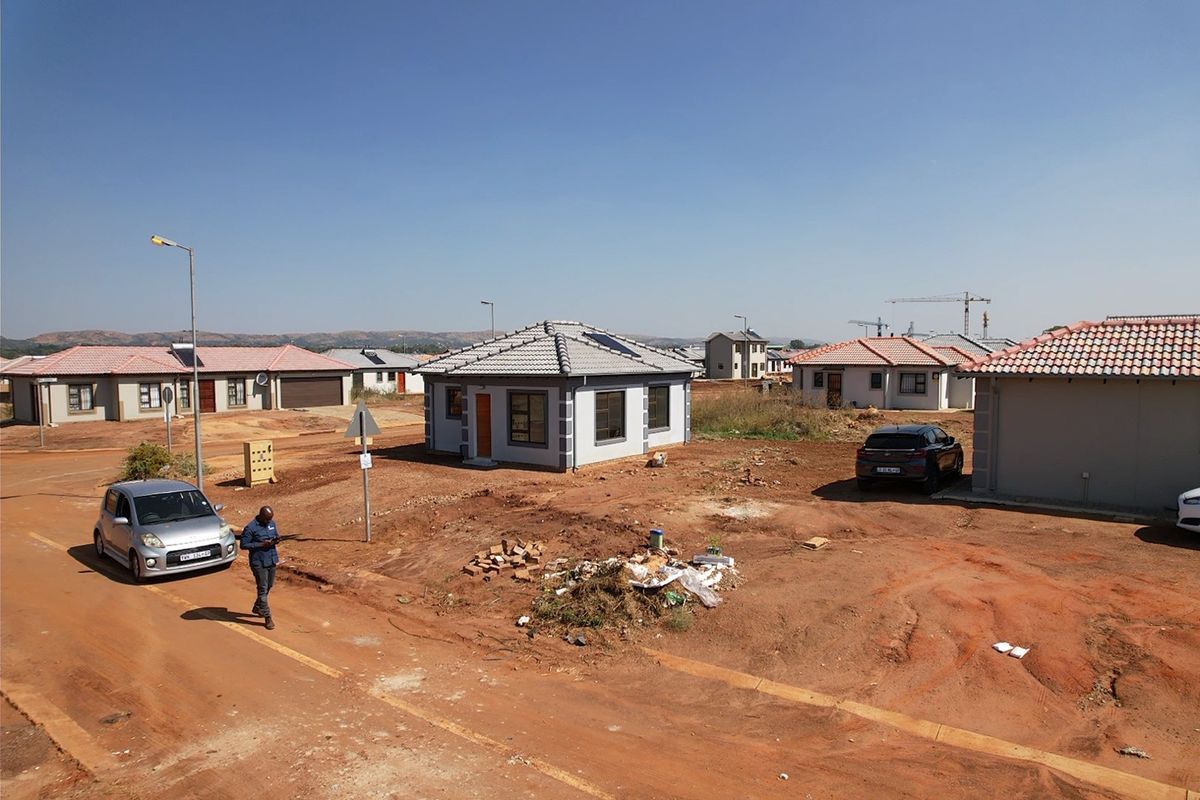 A view of a newly constructed residential property in a developing estate, featuring a tiled roof, solar geyser, and unlandscaped surrounding grounds.