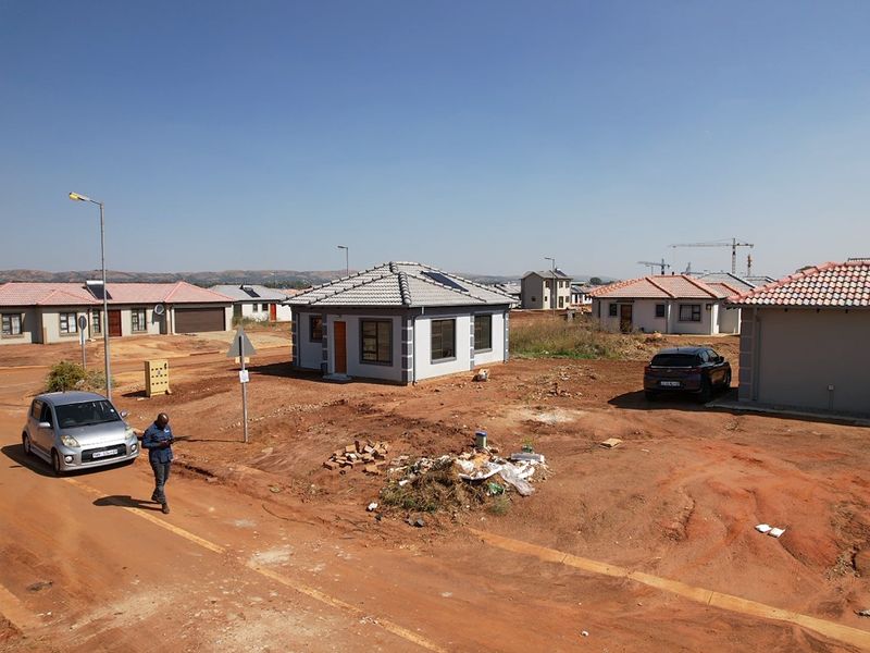 A view of a newly constructed residential property in a developing estate, featuring a tiled roof, solar geyser, and unlandscaped surrounding grounds.