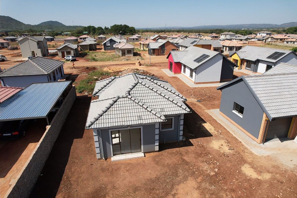 Aerial view of a residential development featuring modern detached houses with tiled roofs, solar panels, and unlandscaped garden plots.