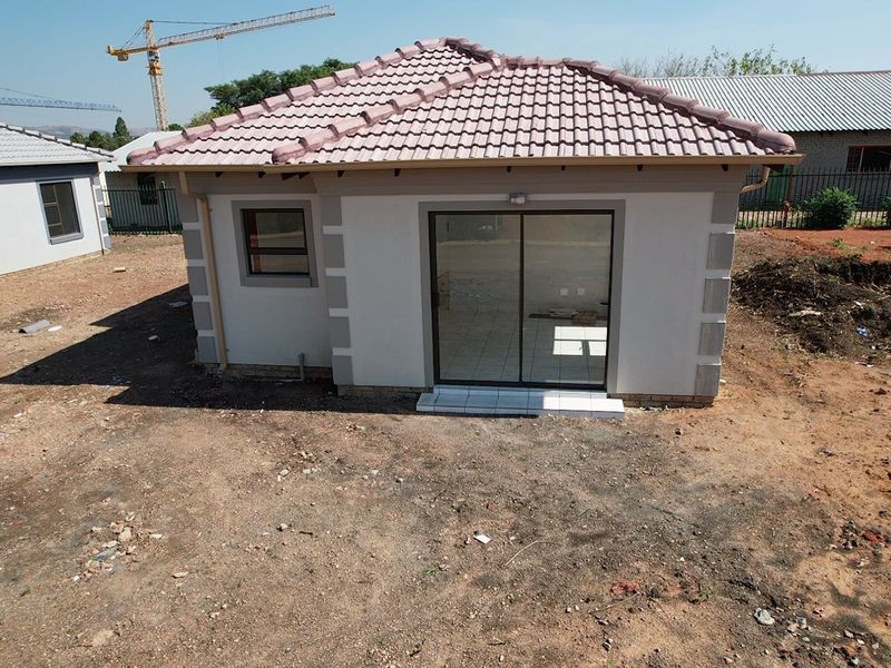 Rear view of a modern single-story house featuring a tiled roof, sliding glass door, and unlandscaped surrounding grounds.