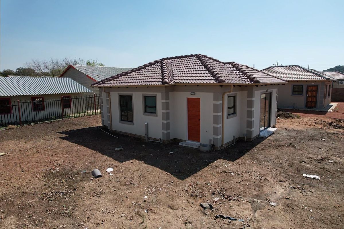 Rear view of a detached house featuring a tiled roof, aluminium window frames, and a sliding door, set on an unlandscaped plot.