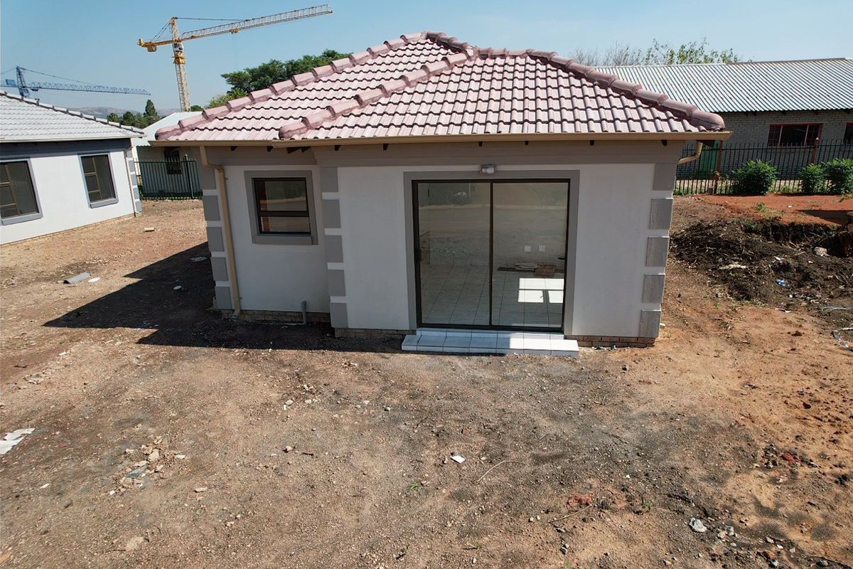Rear view of a modern single-story house featuring a tiled roof, sliding glass door, and unlandscaped surrounding grounds.