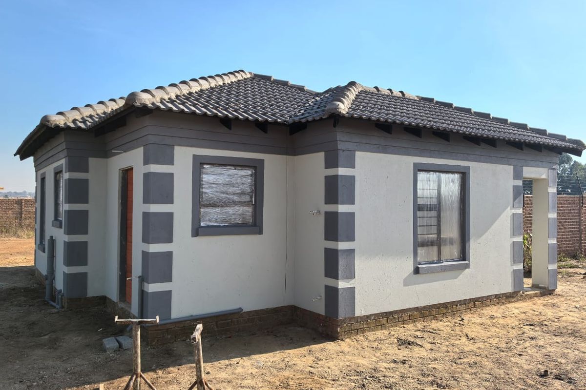 A newly constructed single-story house featuring a tiled roof, plastered exterior walls with contrasting corner detailing, and aluminium window frames.