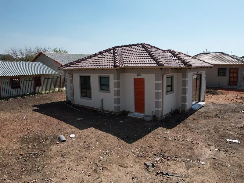 Rear view of a detached house featuring a tiled roof, aluminium window frames, and a sliding door, set on an unlandscaped plot.