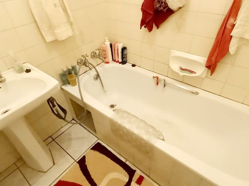 A dated bathroom featuring a pedestal washbasin and a standard bathtub with wall-mounted fixtures, finished with ceramic wall and floor tiling.
