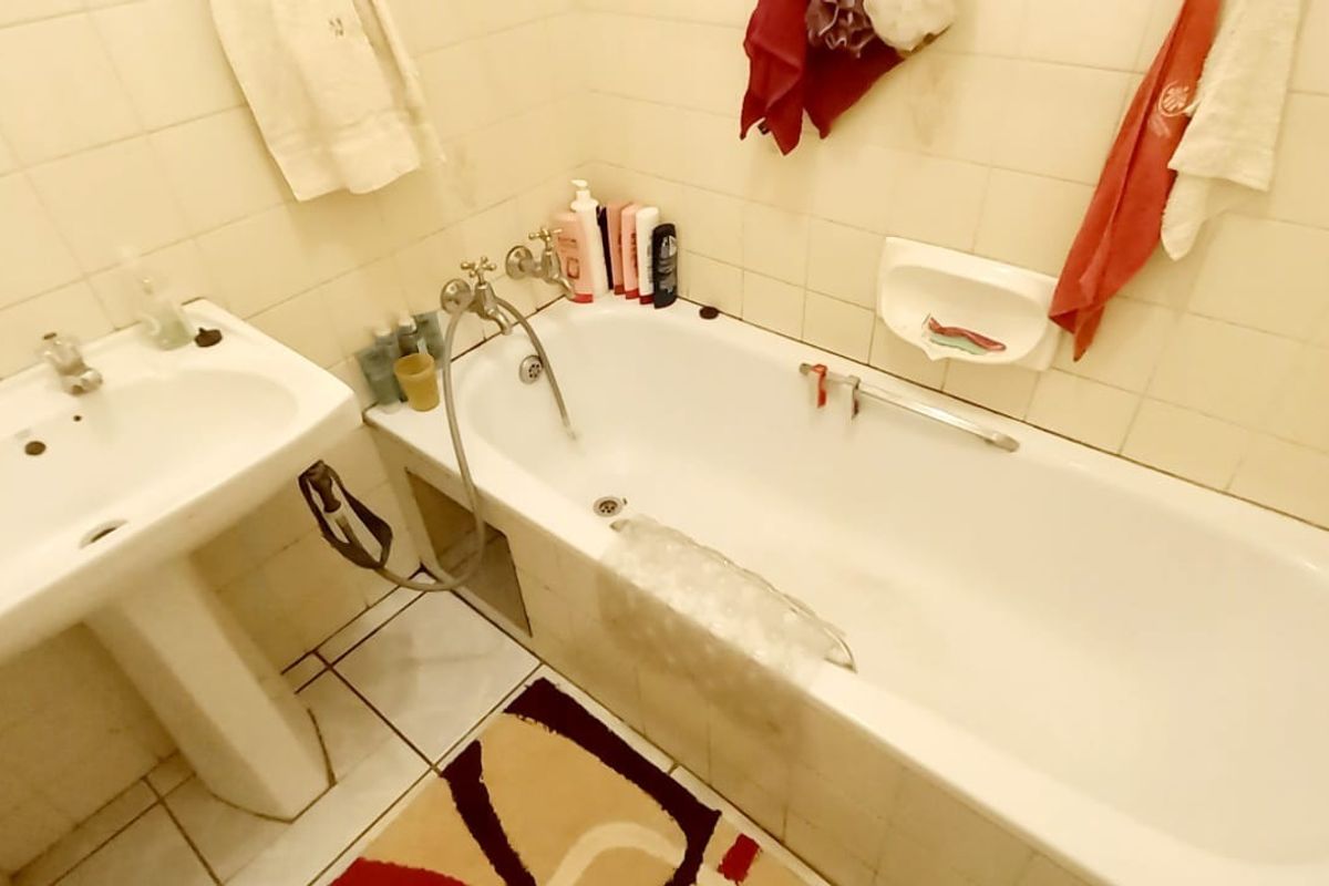 A dated bathroom featuring a pedestal washbasin and a standard bathtub with wall-mounted fixtures, finished with ceramic wall and floor tiling.