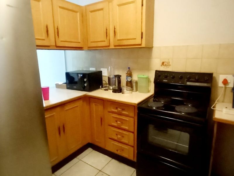 A functional kitchen featuring wooden cabinetry, tiled backsplash, and a freestanding stove, offering a dated aesthetic with potential for modern updates.