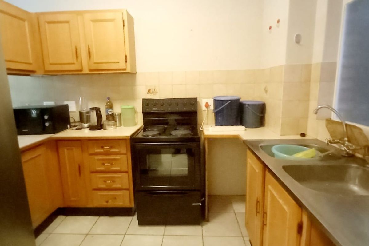 A functional kitchen featuring wooden cabinetry, a freestanding stove, and a double basin sink with tiled backsplash and flooring.