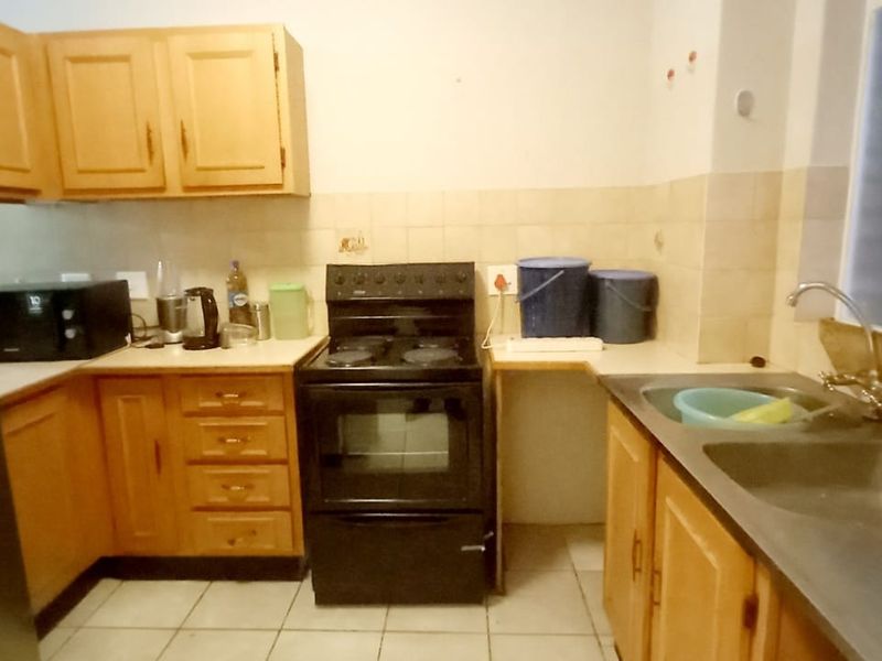 A functional kitchen featuring wooden cabinetry, a freestanding stove, and a double basin sink with tiled backsplash and flooring.