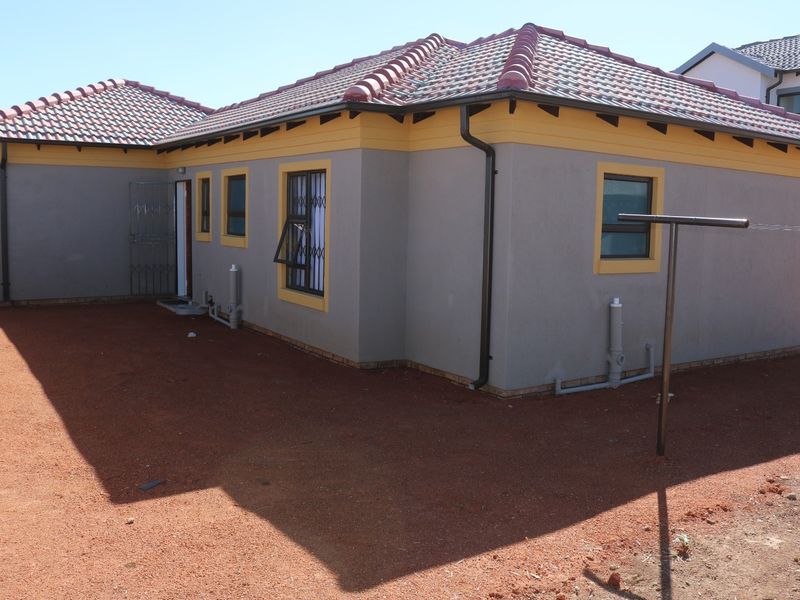 Rear view of a modern house featuring a tiled roof, grey exterior walls with yellow trim, and security gates on windows.