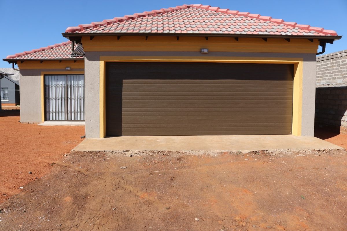 Front view of a residential property featuring a single garage door, tiled roof, and security gate, with unfinished landscaping in the foreground.