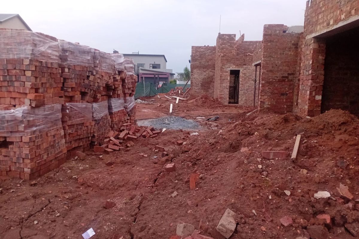 A construction site showing the early stages of a brick house build with exposed masonry and unfinished ground works.
