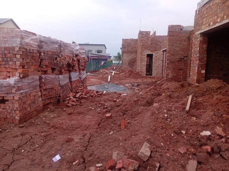 A construction site showing the early stages of a brick house build with exposed masonry and unfinished ground works.