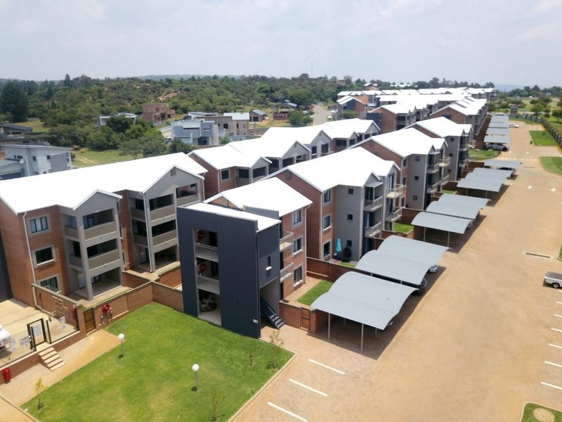 Aerial view of a modern apartment complex featuring multiple residential blocks, covered parking bays, and well-maintained communal garden areas.