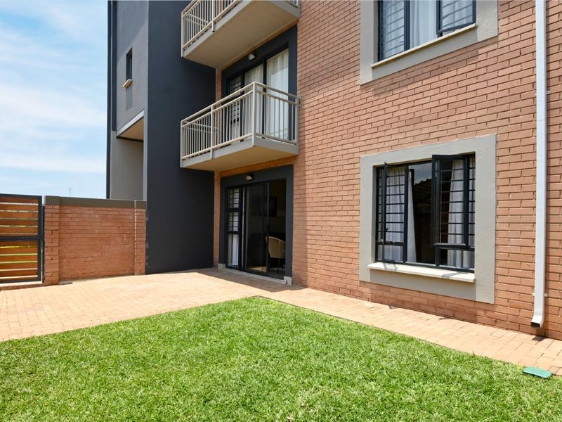 Rear view of the apartment building featuring a private paved patio, small lawn area, and access to the ground floor unit via sliding doors.