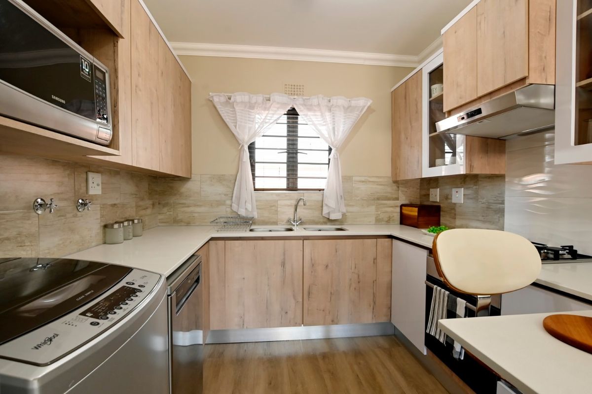 A well-maintained kitchen featuring light wood-finish cabinetry, a double sink, tiled backsplash, and integrated appliances including an extractor fan and built-in microwave.