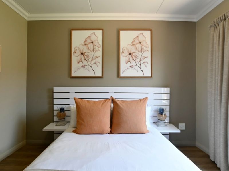 A well-maintained bedroom featuring neutral wall tones, crown molding, laminate flooring, and a custom built-in headboard with integrated bedside shelving.