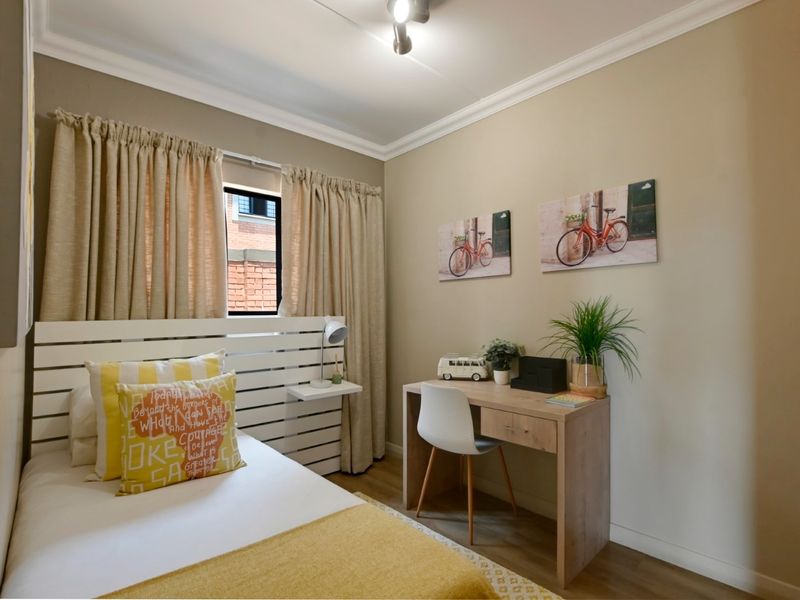 A well-maintained bedroom featuring laminate flooring, coving, and a window with neutral wall tones.