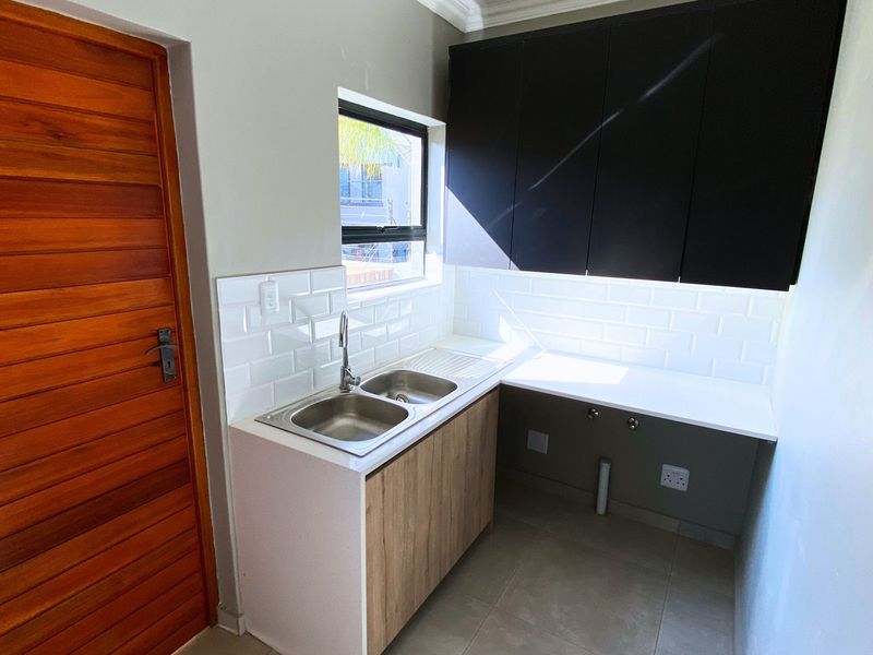 A clean and modern laundry area featuring a double stainless steel sink, subway tile backsplash, and ample built-in cabinetry for storage.