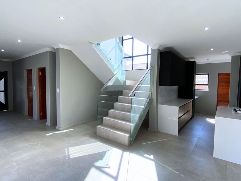 Spacious open-plan living area featuring a modern staircase with glass balustrade, sleek kitchen cabinetry, and a central island with a built-in gas hob.