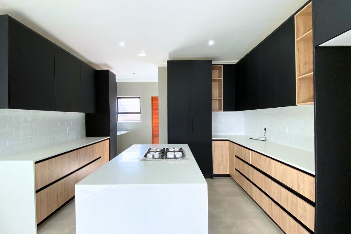 Modern kitchen featuring sleek black and wood-tone cabinetry, a central island with a gas cooktop, stone countertops, and a classic subway tile backsplash.