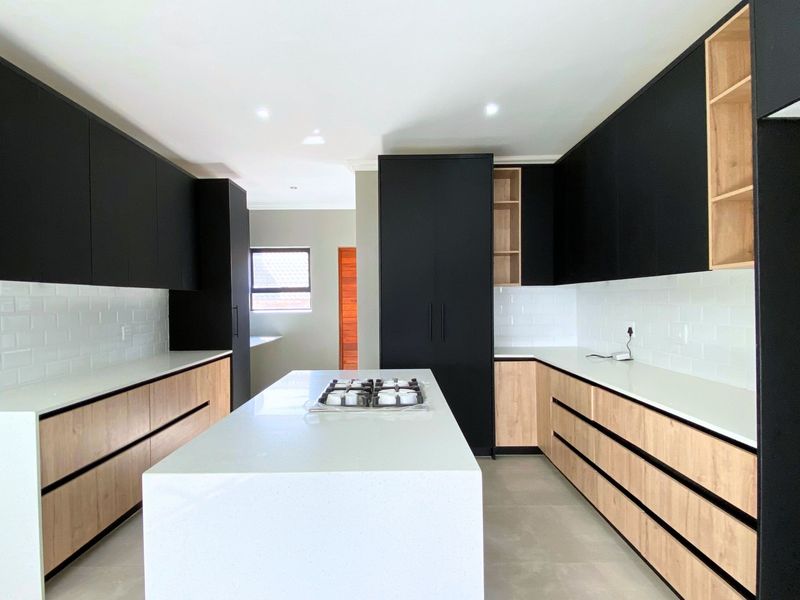 Modern kitchen featuring sleek black and wood-tone cabinetry, a central island with a gas cooktop, stone countertops, and a classic subway tile backsplash.
