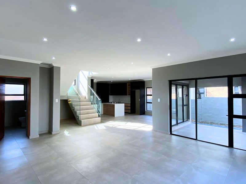 Spacious open-plan living area featuring modern tiled floors, recessed lighting, a contemporary glass staircase, and seamless access to the outdoor patio.